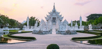 Sunset colors the garden and beautiful whites of Wat Rong Khun, Chiang Rai's famous white temple in northern Thailand