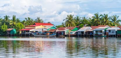 Riverside village has multi coloured houses built right on the river, with barges parked next to them and slightly clouded blue skies