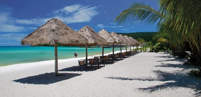 White-sand beach lined with straw-thatched umbrellas next to azure waters in Cambodia's coast.