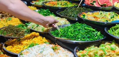 Person grabs food from a buffet filled with vegetables using chopsticks in Luang Prabang, Laos