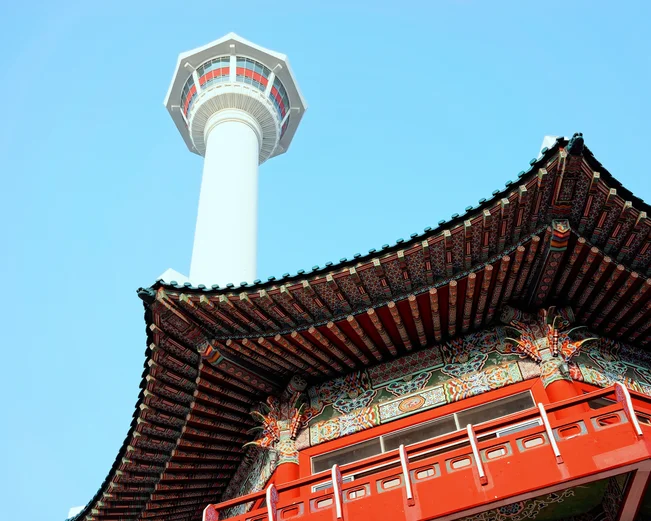 Ornate red temple roof with white Busan Tower in background