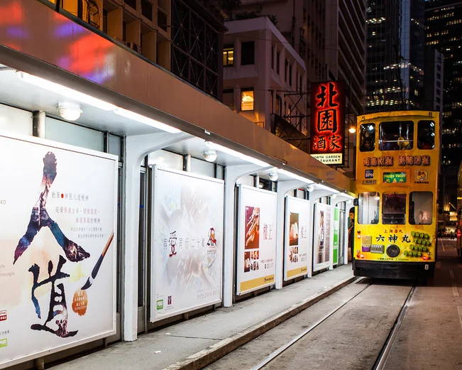 Yellow tram travelling along tracks alongside advertisements at night 