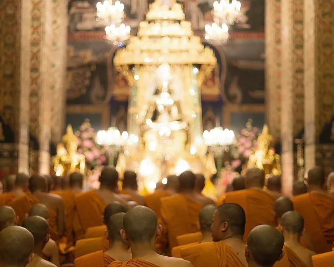 Monks kneeling and praying inside illuminated temple in Bangkok