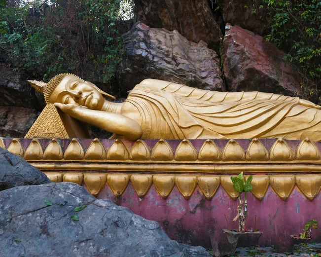 Reclining gold gilt buddha on purple platform surrounded by craggy rocks
