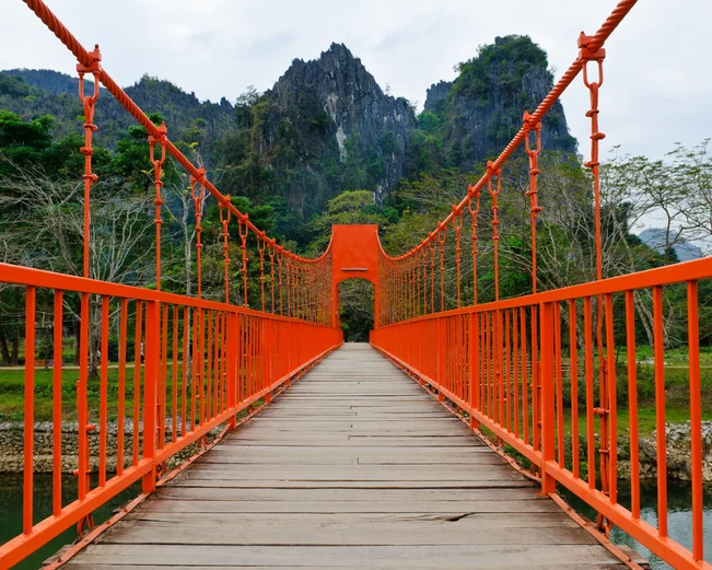 Red foot bridge with dramatic mountain scenery in background