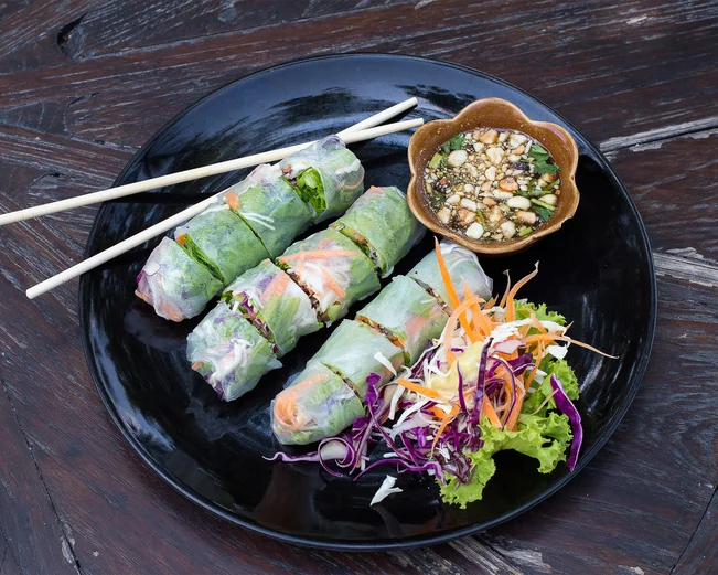 Delicious Vietnamese rice paper spring rolls sit in a dish on a wooden table