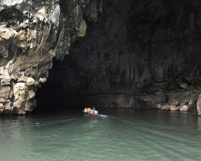 Small boat with people entering the massive Tham Kong Lo cave on calm, dark cave waters
