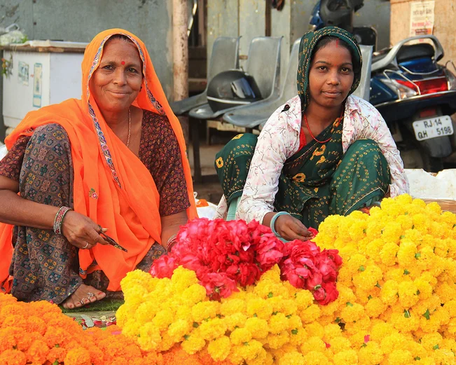 two women selling orange, red and yellow flowers