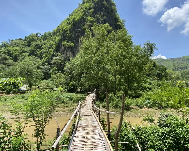 A bamboo bridge leading to a tree-covered hill in Nong Khiaw