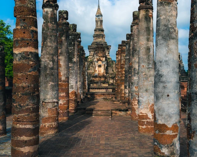 A path between ruined pillars, leading towards a stupa in the middle
