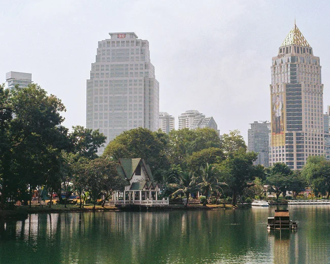 A boat cruises over the pond in Lumphini Park, with skycrapers in the background