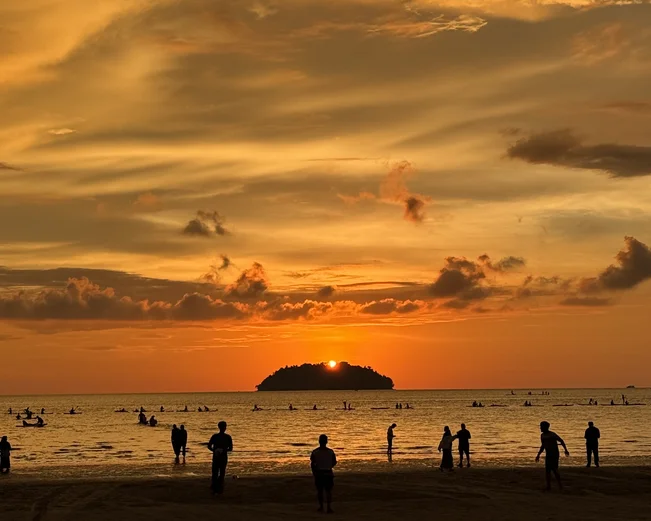 People on a beach silhouetted by an orange sunset