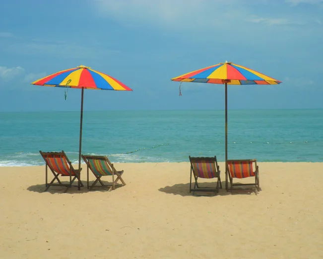 Four deckchairs sit under two rainbow parasols