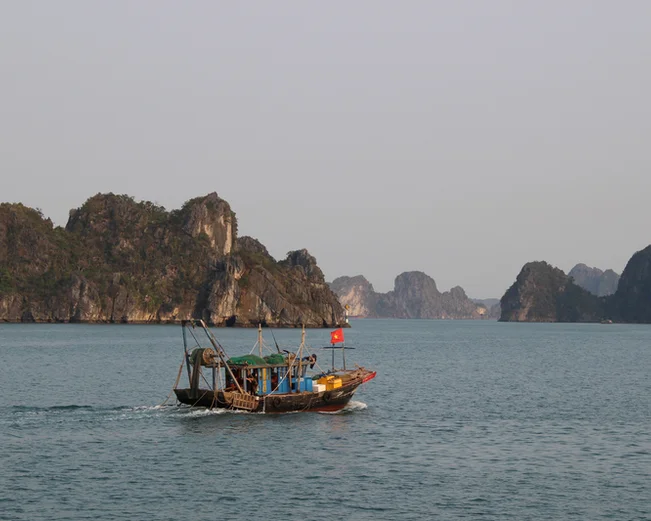 A fishing boat crosses a calm sea with limestone karsts in the background