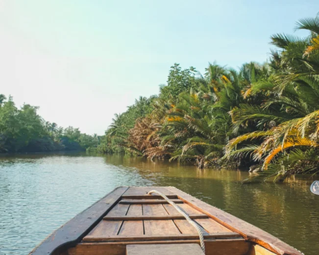 The prow of a wooden boat, looking over a river passing between two green banks
