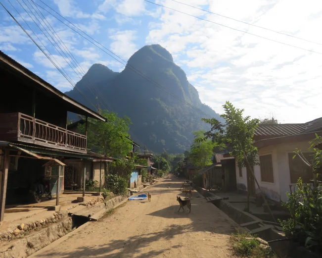 a dust path between two stilted houses leads to a forested karst