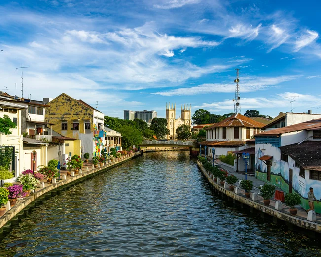 river with lowrise buildings either side. A white church can be seen in the background