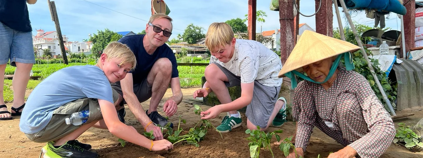 A father and his two young sons planting vegetables with a local farmer at an experience in Vietnam