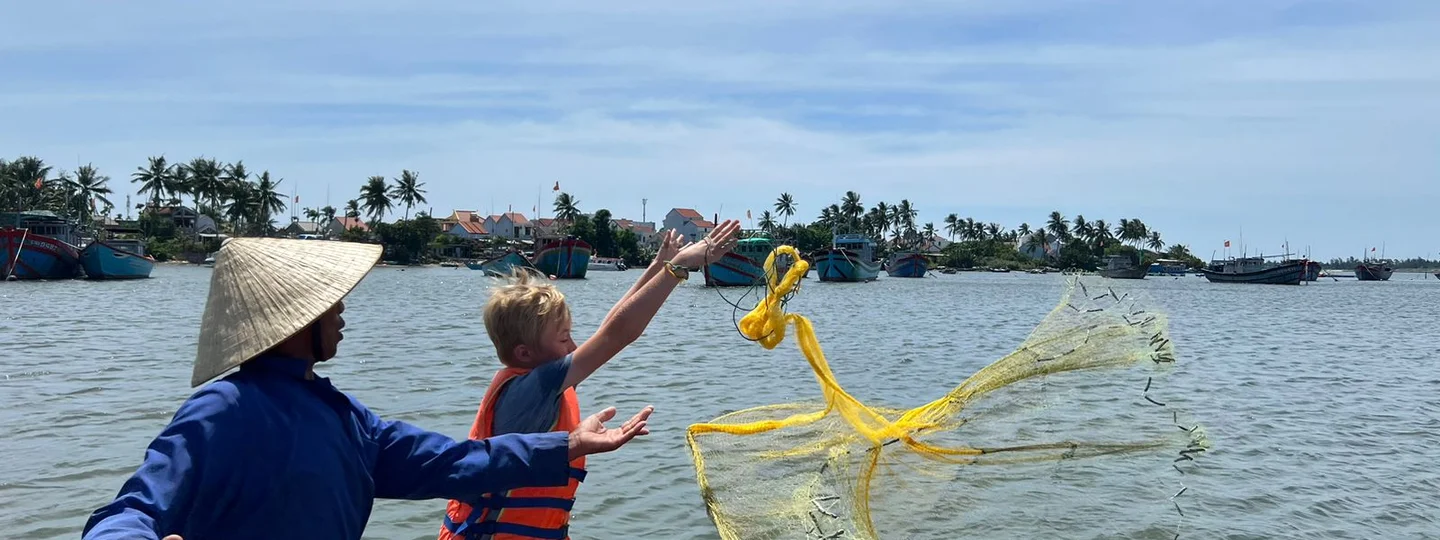 A young boy throwing a fishing net into the water with a local fisherman on a traditional experience in Vietnam