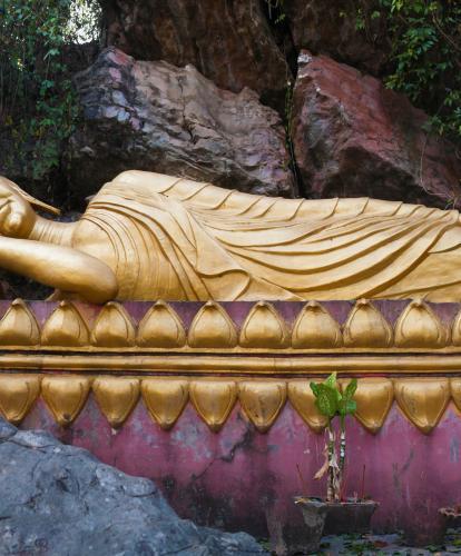 Reclining gold gilt buddha on purple platform surrounded by craggy rocks