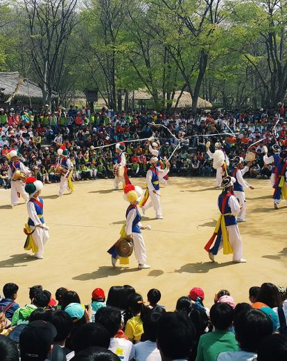 Dancers in traditional costume in circle surrounded by crowds of spectators