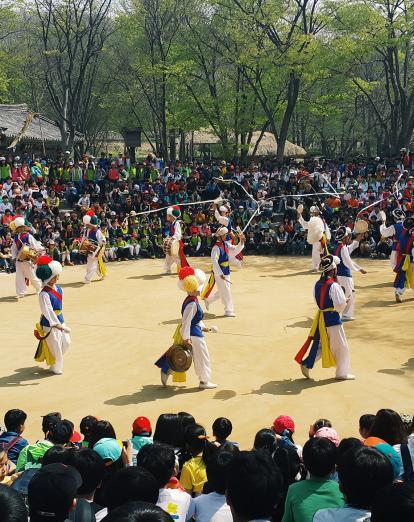 Dancers in traditional costume in circle surrounded by crowds of spectators 