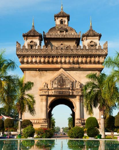 Arch monument in Vientiane with palm trees and water in the foreground