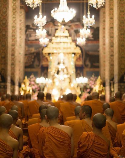 Monks kneeling and praying inside illuminated temple in Bangkok