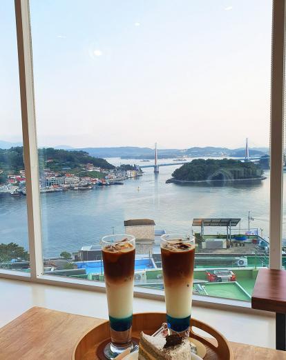 Tall iced coffee drinks and cake on a tray overlooking Yeosu seaside