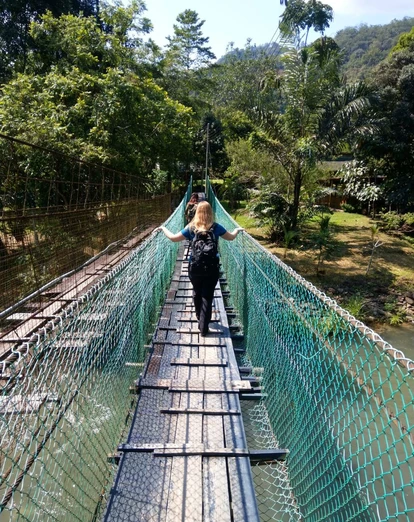 Woman crossing a narrow suspension bridge over a river in a tropical forest, wearing a backpack