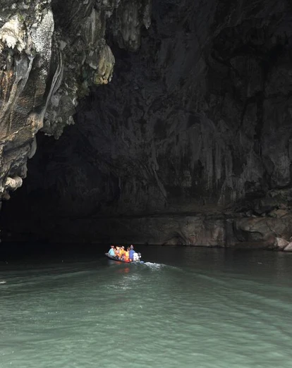 Small boat with people entering the massive Tham Kong Lo cave on calm, dark cave waters