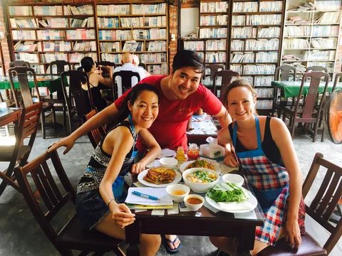 Two friends smiling with a waiter in Vietnamese restaurant 