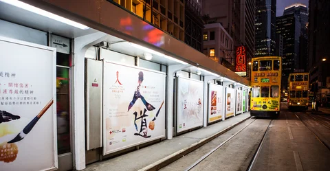 Yellow tram travelling along tracks alongside advertisements at night 