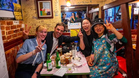 A group of people posing with peace signs at a table filled with food and drinks