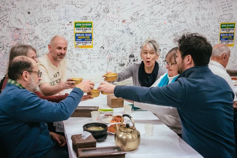 Group enjoying traditional Korean meal with brass bowls and teapot in a vibrant restaurant covered in handwritten notes
