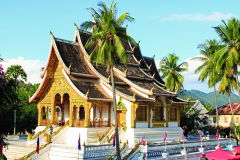 White temple with sloped roof and gold walls in Luang Prabang surrounded by palm trees at a quiet hour