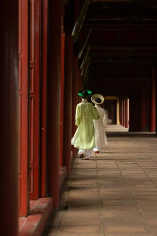 Two Vietnamese women in traditional dress in front of the red doors of the palace in Hue
