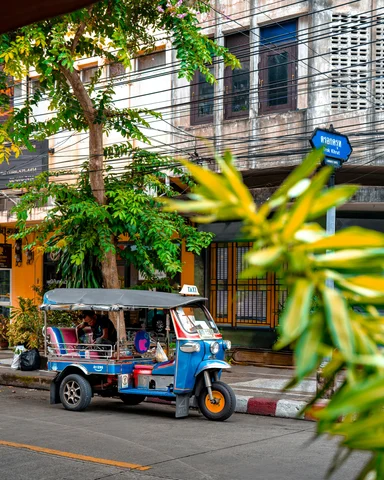 A tuk tuk parked up along the side of the road, with shops behind