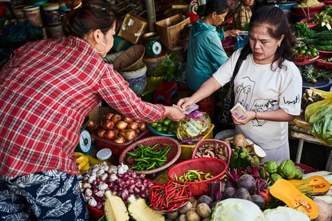 Two women completing a purchase for vegetables at a market stall