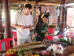 Travel consultant with a local preparing traditional food in a rustic kitchen with fresh fruits and bamboo sticks on the table