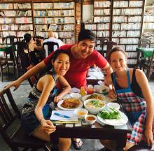 Two friends smiling with a waiter in Vietnamese restaurant 