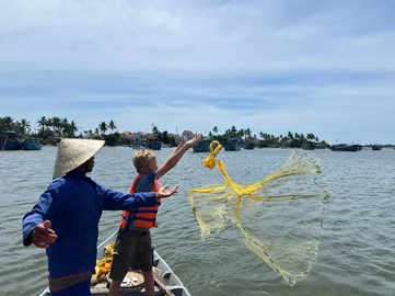 A child throwing a fishing net into the sea during an experience with a local on a family holiday adventure in Southeast Asia