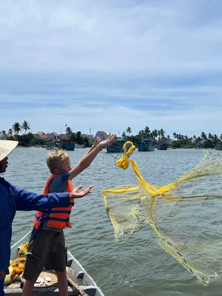 A child throwing a fishing net into the sea during an experience with a local on a family holiday adventure in Southeast Asia