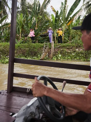 A local Vietnamese boat driver on the Mekong Delta being waved to by women in the jungle on a boat cruise