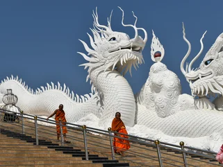 Monks walking down temple steps in traditional clothes in front of giant white dragon sculptures