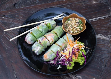 Delicious Vietnamese rice paper spring rolls sit in a dish on a wooden table