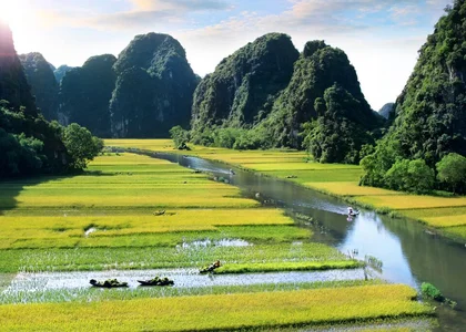 Panoramic landscape of Ninh Binh in Vietnam with vibrant rice fields, calm river, and dramatic limestone cliffs surrounded by greenery