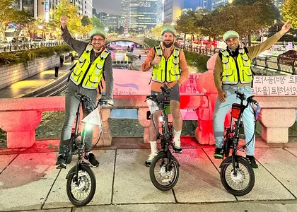 3 men on e-bikes posing in front of Cheonggyecheon stream