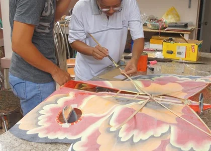 A man makes a kite of an orange and yellow butterfly out of silk and bamboo