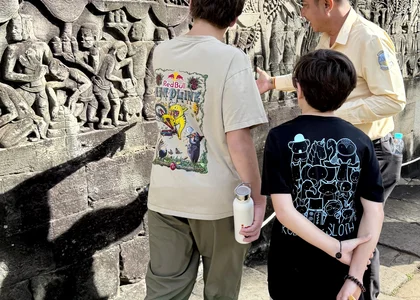 Two teenaged boys look at the murals on a temple wall with their guide